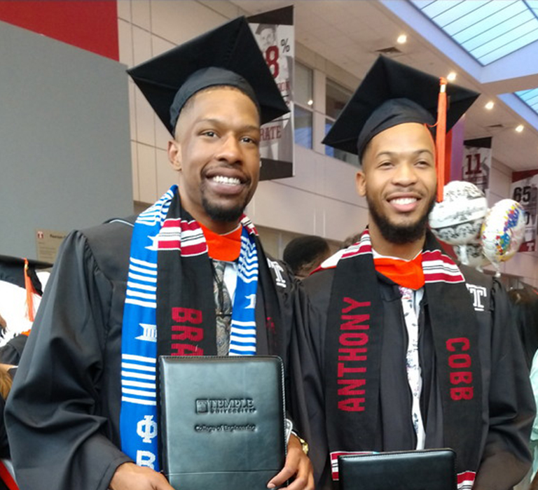 2 smiling men in graduation gowns